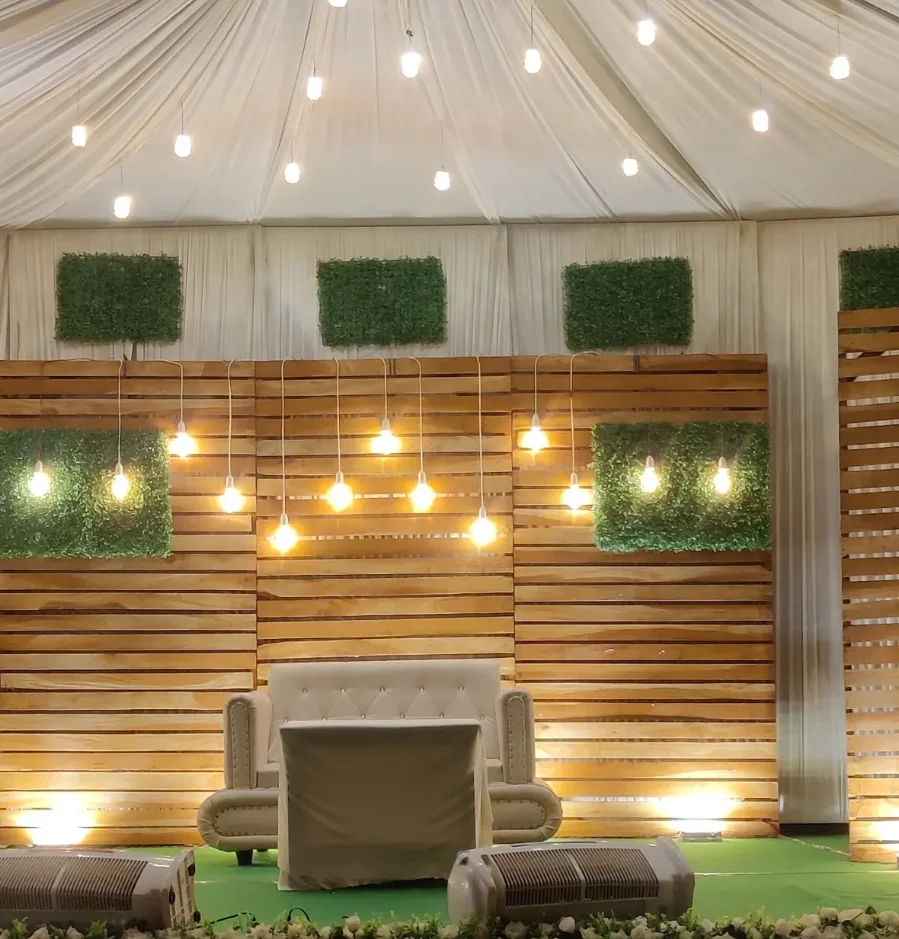 Wooden-slat wedding stage decoration with hanging lights and greenery panels